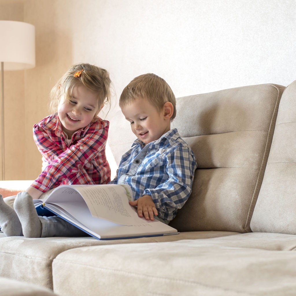 The cute little brother and sister reading a book together on the couch at home